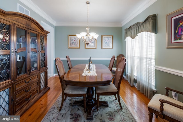 dining space with ornamental molding, wood-type flooring, and a notable chandelier