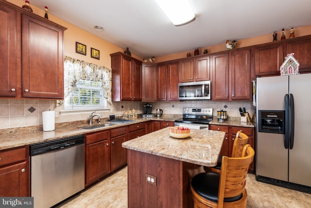 kitchen featuring appliances with stainless steel finishes, light stone counters, a breakfast bar, sink, and a kitchen island