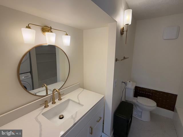 bathroom with vanity, washer / dryer, and toilet