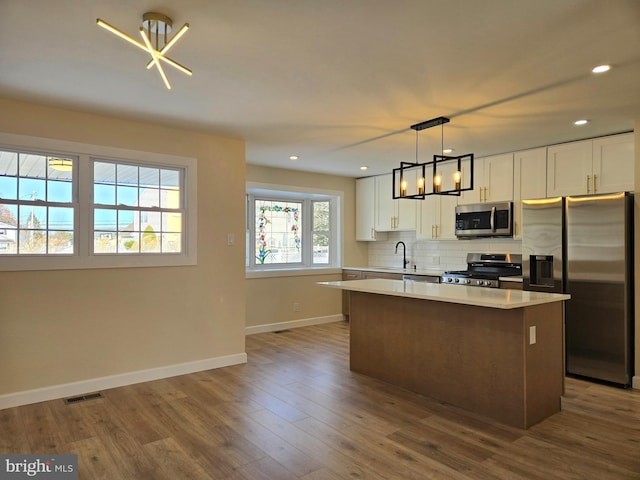 kitchen with white cabinetry, sink, decorative light fixtures, a kitchen island, and appliances with stainless steel finishes