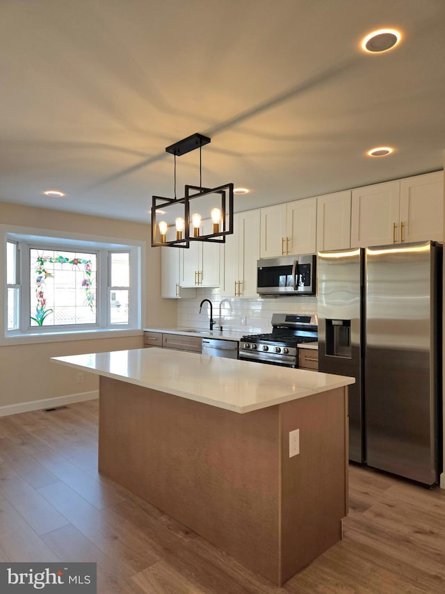 kitchen with a kitchen island, white cabinets, pendant lighting, and appliances with stainless steel finishes