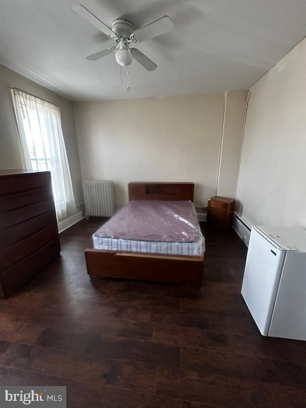 bedroom with radiator heating unit, a baseboard radiator, ceiling fan, and dark wood-type flooring