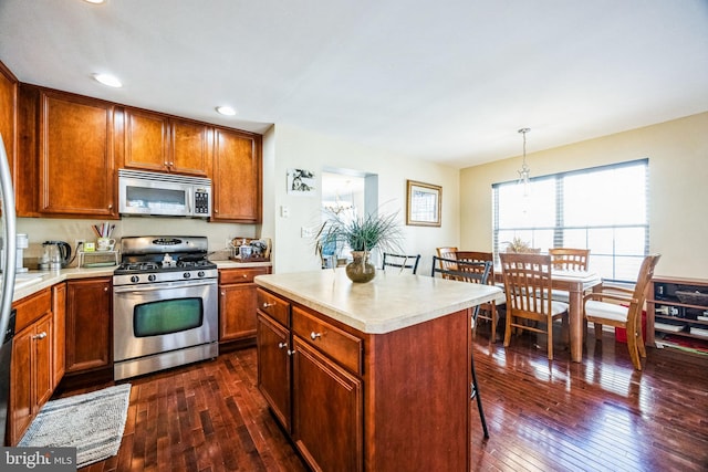 kitchen with dark hardwood / wood-style flooring, decorative light fixtures, a breakfast bar area, a kitchen island, and appliances with stainless steel finishes