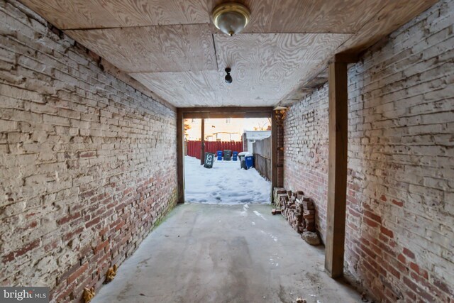 hallway with brick wall, concrete floors, and wooden ceiling