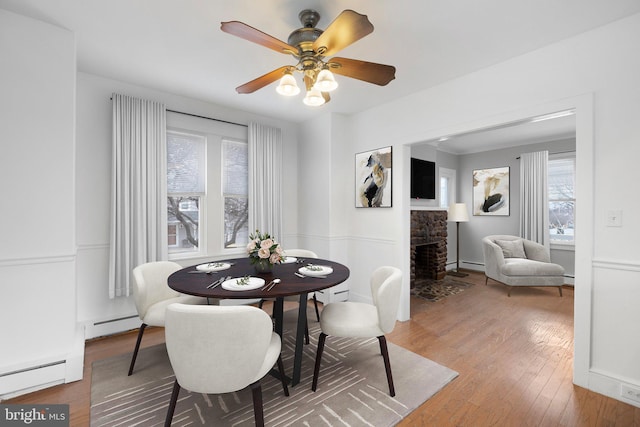 dining area featuring a fireplace, wood-type flooring, plenty of natural light, and ceiling fan