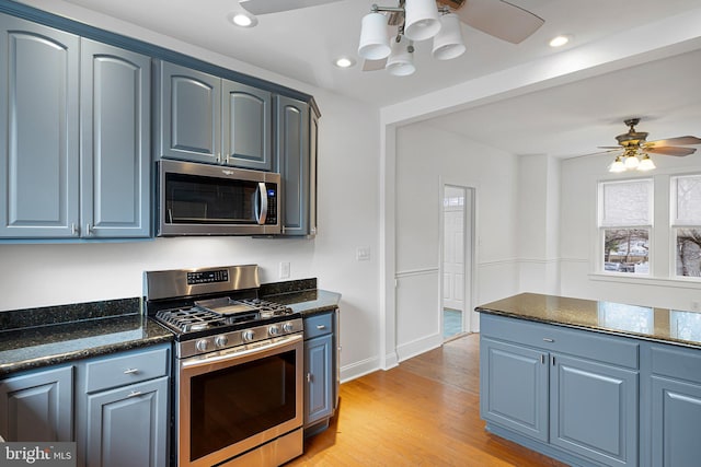 kitchen with appliances with stainless steel finishes, dark stone counters, ceiling fan, blue cabinetry, and light hardwood / wood-style floors