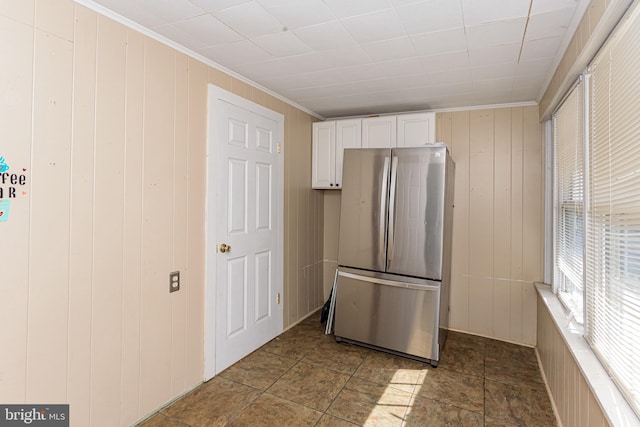 kitchen with white cabinetry, ornamental molding, stainless steel fridge, and wooden walls