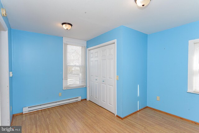 unfurnished bedroom featuring a closet, a baseboard heating unit, and light hardwood / wood-style flooring