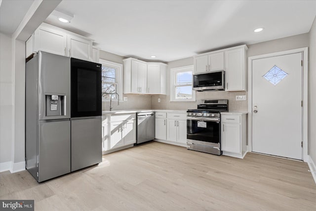 kitchen featuring white cabinetry, appliances with stainless steel finishes, backsplash, and light wood-type flooring