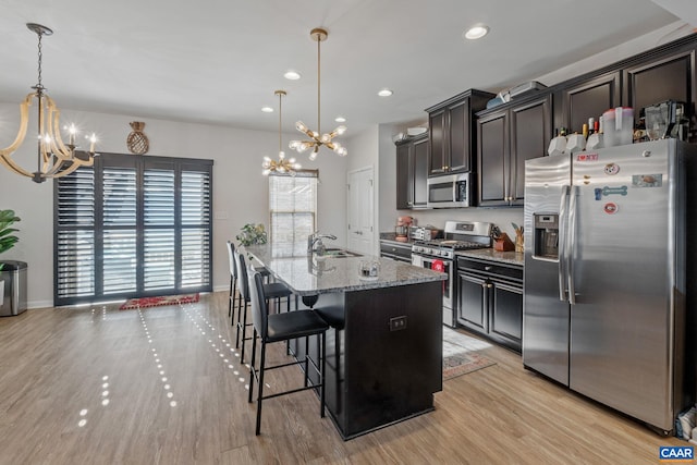 kitchen with a kitchen island with sink, a kitchen breakfast bar, hanging light fixtures, light stone counters, and stainless steel appliances