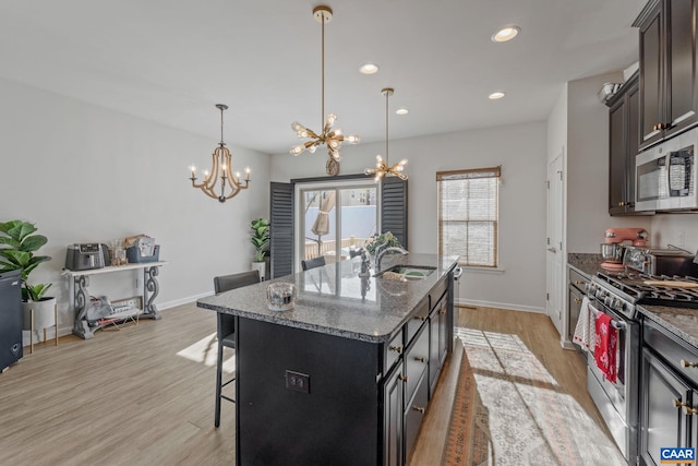 kitchen featuring an island with sink, appliances with stainless steel finishes, light hardwood / wood-style floors, a breakfast bar area, and a chandelier