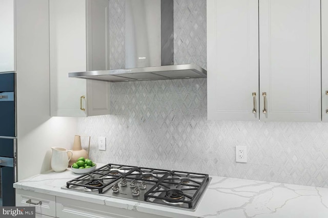 kitchen featuring light stone countertops, decorative backsplash, stainless steel gas cooktop, wall chimney range hood, and white cabinets