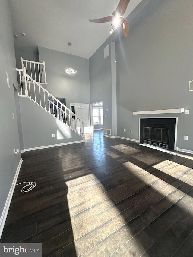 unfurnished living room with ceiling fan, a towering ceiling, and dark hardwood / wood-style floors