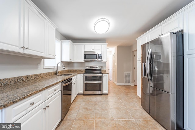 kitchen with white cabinetry, sink, dark stone countertops, light tile patterned floors, and stainless steel appliances