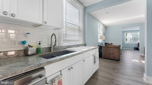 kitchen with stainless steel dishwasher, light stone countertops, sink, and white cabinets