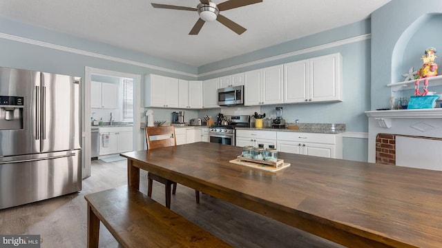 kitchen with sink, white cabinetry, appliances with stainless steel finishes, hardwood / wood-style flooring, and dark stone counters