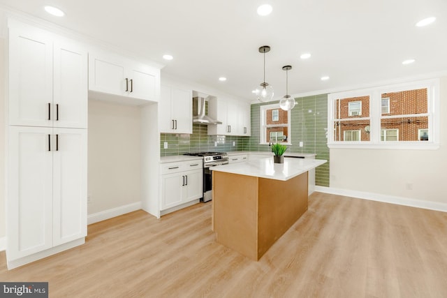 kitchen featuring wall chimney range hood, pendant lighting, light hardwood / wood-style flooring, white cabinets, and stainless steel range with gas cooktop