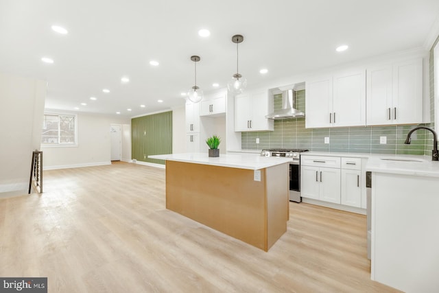 kitchen with a center island, wall chimney range hood, sink, stainless steel gas stove, and white cabinetry