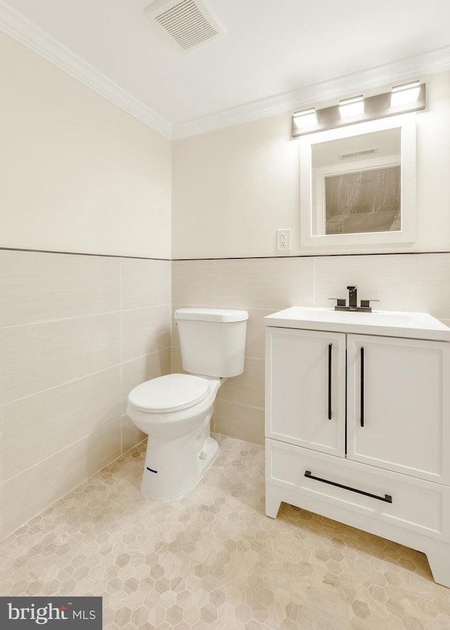 bathroom featuring vanity, toilet, ornamental molding, and tile walls