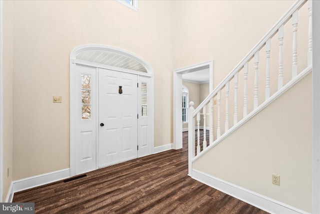 foyer entrance featuring dark wood-type flooring, a towering ceiling, and a healthy amount of sunlight