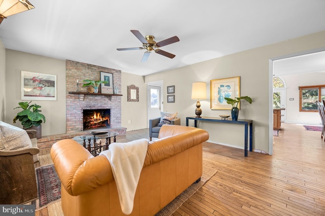 living room featuring ceiling fan, light hardwood / wood-style floors, and a brick fireplace