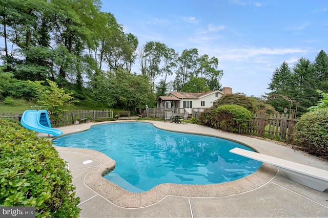 view of swimming pool featuring a diving board, a water slide, and a patio