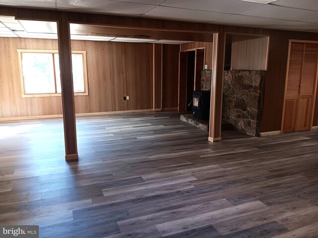 basement with a wood stove, wood walls, and dark wood-type flooring