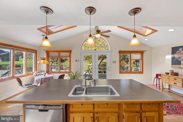 kitchen featuring lofted ceiling with skylight, sink, dishwasher, hanging light fixtures, and an island with sink