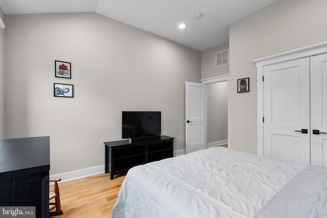 bedroom with vaulted ceiling, light wood-type flooring, and a closet