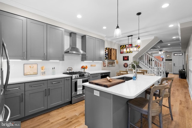 kitchen featuring gray cabinetry, sink, wall chimney exhaust hood, a kitchen island with sink, and appliances with stainless steel finishes