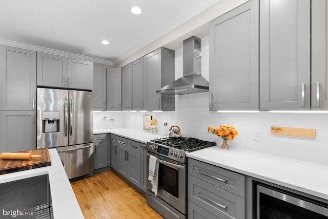 kitchen with gray cabinetry, light stone countertops, wall chimney exhaust hood, stainless steel appliances, and light wood-type flooring