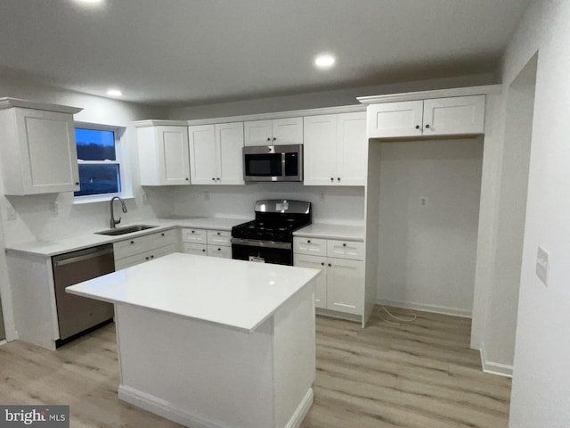 kitchen with stainless steel appliances, sink, white cabinets, a center island, and light hardwood / wood-style floors