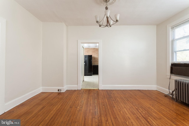 spare room with a notable chandelier, light hardwood / wood-style floors, and radiator