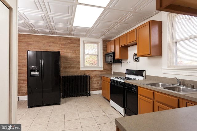 kitchen with radiator heating unit, sink, brick wall, light tile patterned floors, and black appliances