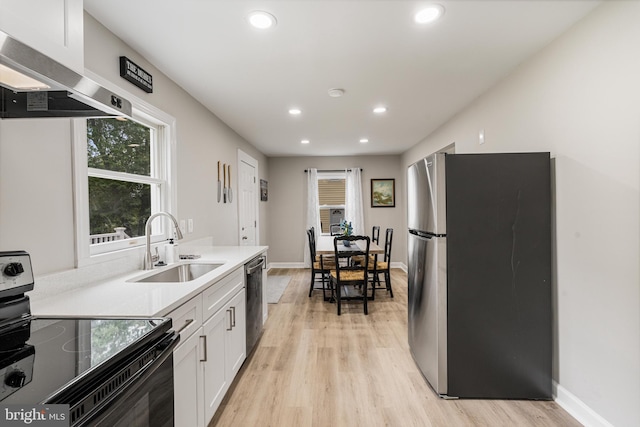 kitchen featuring white cabinets, sink, light wood-type flooring, range hood, and appliances with stainless steel finishes