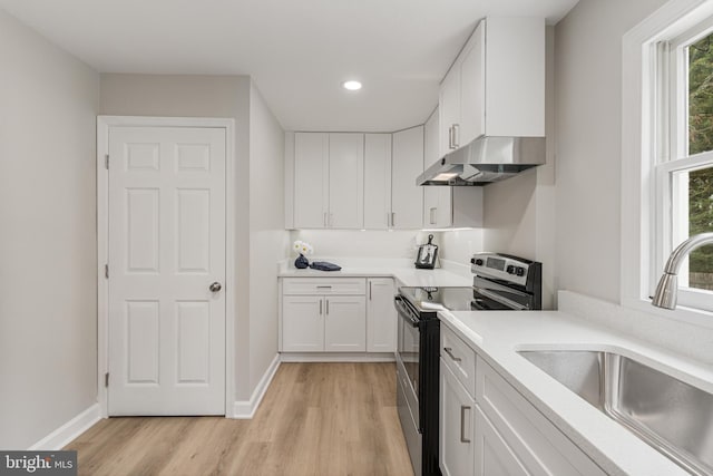 kitchen featuring electric range, sink, white cabinets, and light hardwood / wood-style flooring