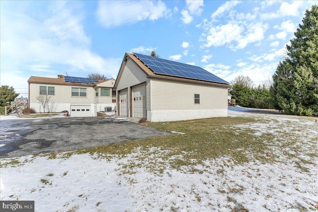 snow covered back of property featuring solar panels and a garage