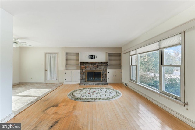 unfurnished living room with ceiling fan, light wood-type flooring, built in features, and a fireplace