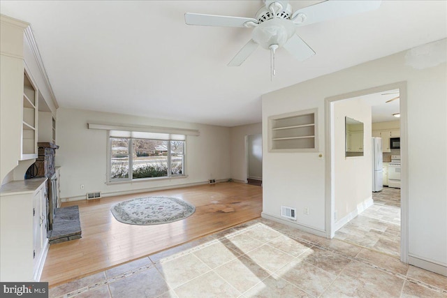 unfurnished living room featuring built in shelves, ceiling fan, and light wood-type flooring