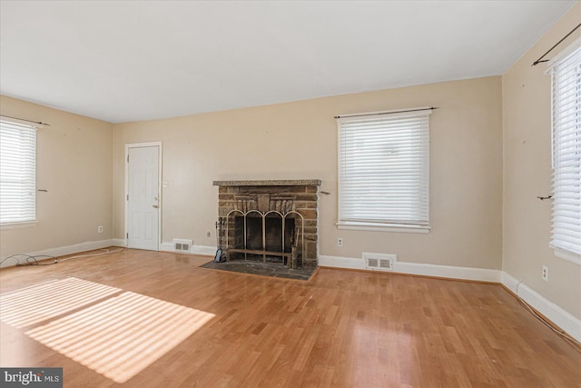 unfurnished living room with hardwood / wood-style flooring, a healthy amount of sunlight, and a stone fireplace