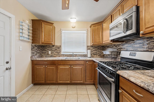 kitchen with sink, light tile patterned floors, backsplash, stainless steel appliances, and light stone countertops