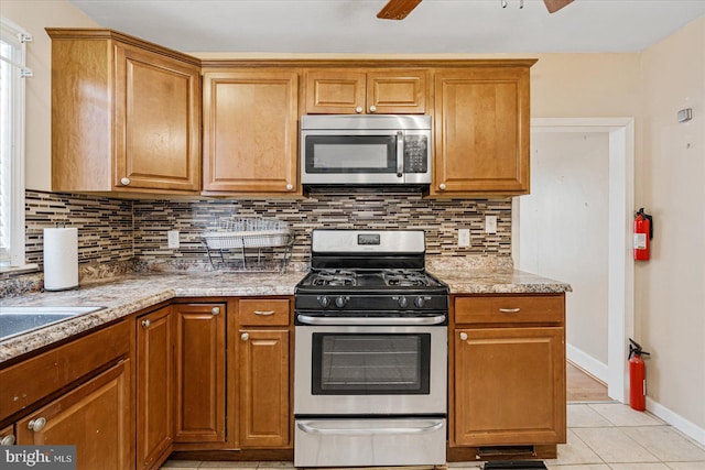 kitchen featuring light tile patterned flooring, light stone counters, ceiling fan, stainless steel appliances, and decorative backsplash