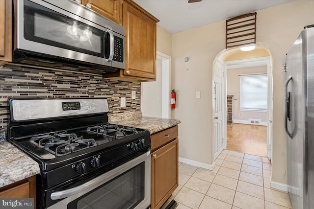 kitchen with tasteful backsplash, light stone countertops, light tile patterned floors, and stainless steel appliances