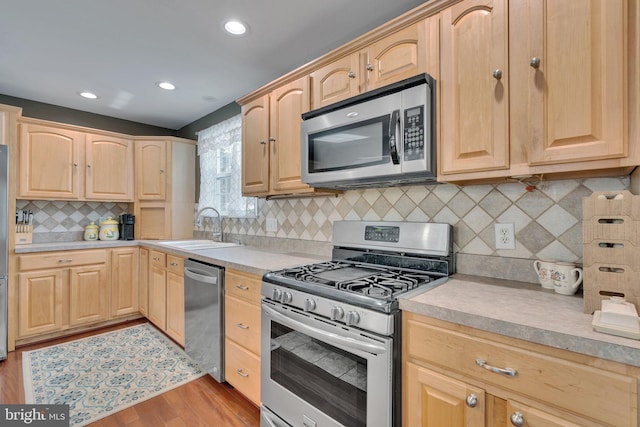 kitchen with stainless steel appliances, light brown cabinetry, sink, and light hardwood / wood-style flooring