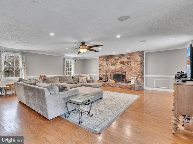 living room featuring crown molding, a brick fireplace, a textured ceiling, and light hardwood / wood-style flooring