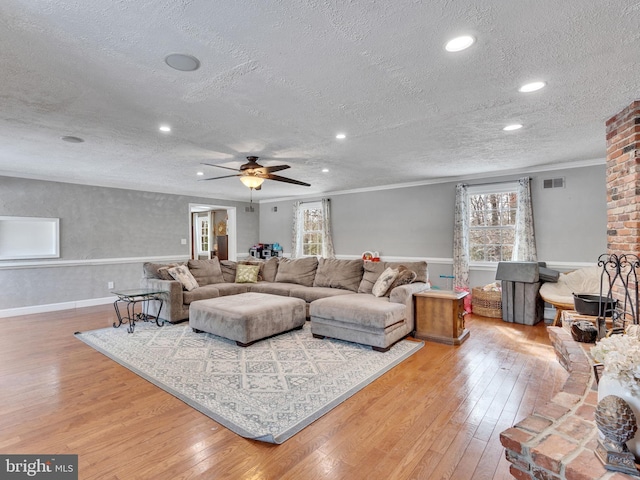 living room featuring hardwood / wood-style flooring, ceiling fan, crown molding, and a textured ceiling