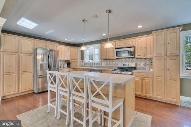 kitchen featuring pendant lighting, stainless steel appliances, a center island, and light brown cabinets