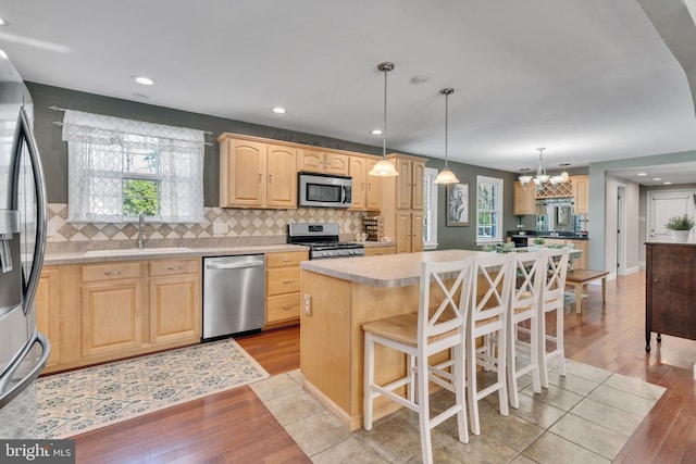 kitchen with pendant lighting, sink, appliances with stainless steel finishes, a kitchen island, and light brown cabinetry