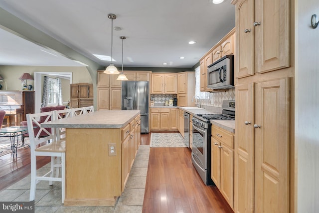 kitchen with a kitchen island, light brown cabinetry, decorative light fixtures, a breakfast bar area, and stainless steel appliances