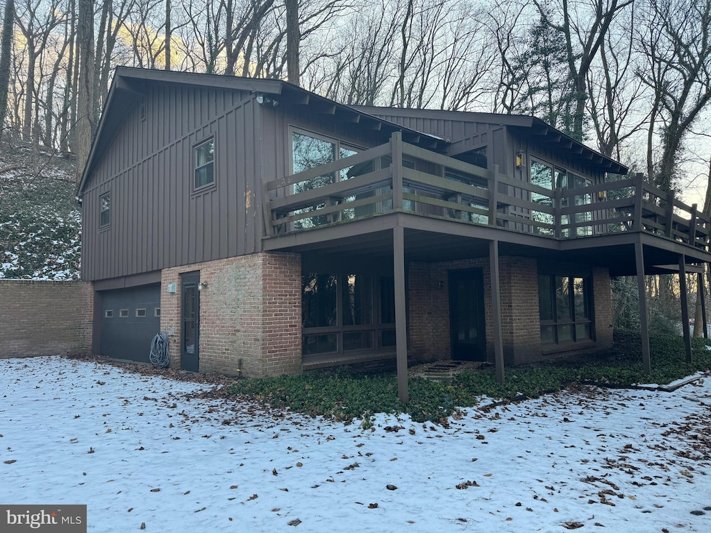 snow covered house featuring a garage and a wooden deck